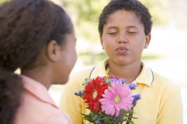 Young boy giving young girl flowers and puckering up clipart