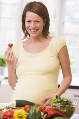 Pregnant woman in kitchen making a salad smiling clipart