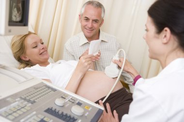 Pregnant woman getting ultrasound from doctor with husband looki clipart