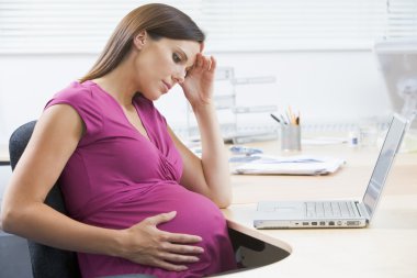 Pregnant woman at work with laptop looking stressed clipart