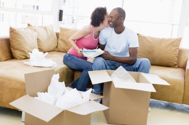 Couple unpacking boxes in new home kissing and smiling clipart