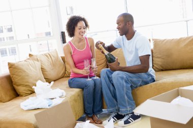 Couple relaxing with champagne by boxes in new home smiling clipart