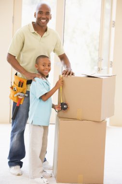 Father wearing tool belt standing by son and boxes in new home s clipart