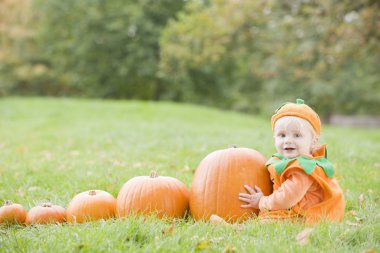 Baby boy outdoors in pumpkin costume with real pumpkins clipart