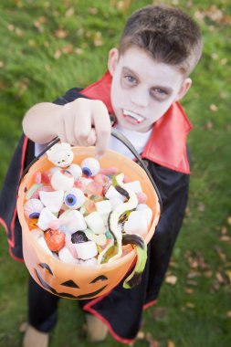 Young boy outdoors wearing vampire costume on Halloween holding clipart