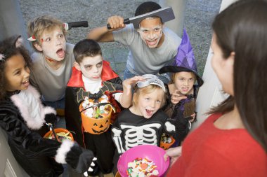 Six children in costumes trick or treating at woman's house clipart