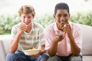 Teenage Boys Sitting On Couch Eating crisps Together clipart