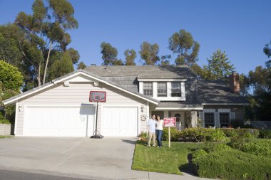 Couple Standing Outside House With Real Estate Sign clipart