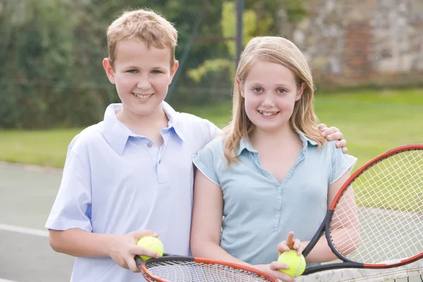 Två unga vänner med racketar på tennis court leende — Stockfoto
