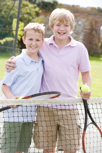 Два молодых друга-мужчины с ракетками на теннисном корте улыбаются — стоковое фото