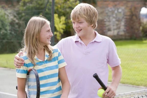 Junges Paar mit Schlägern auf Tennisplatz lächelt — Stockfoto
