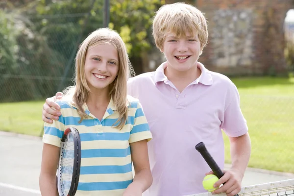 年轻夫妇与球拍上网球法院微笑 — 图库照片