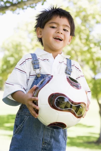 Мальчик держит футбольный мяч на открытом воздухе улыбаясь — стоковое фото