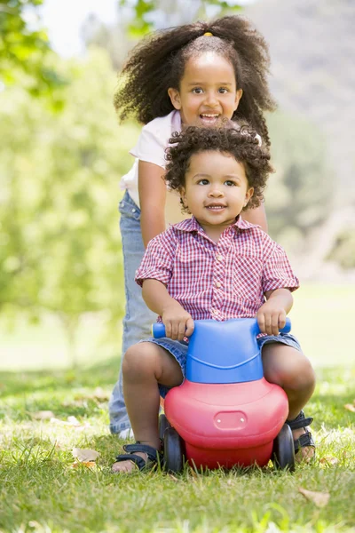 Hermana empujando hermano en juguete con ruedas sonriendo —  Fotos de Stock
