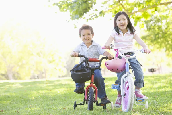 Broer en zus buiten op fietsen glimlachend — Stockfoto