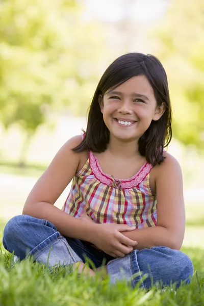 Νεαρή κοπέλα κάθεται χαμογελώντας σε εξωτερικούς χώρους — Φωτογραφία Αρχείου