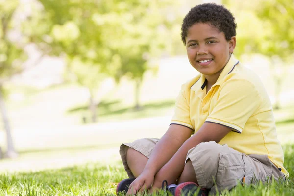 Νεαρό αγόρι κάθεται σε εξωτερικούς χώρους χαμογελώντας — Φωτογραφία Αρχείου