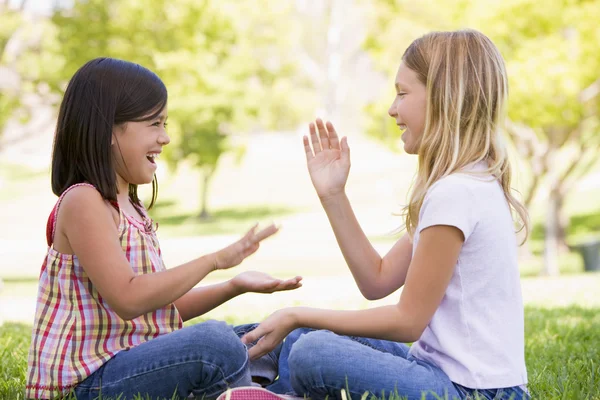 Two young girl friends sitting outdoors playing patty cake smili — Stock Photo, Image