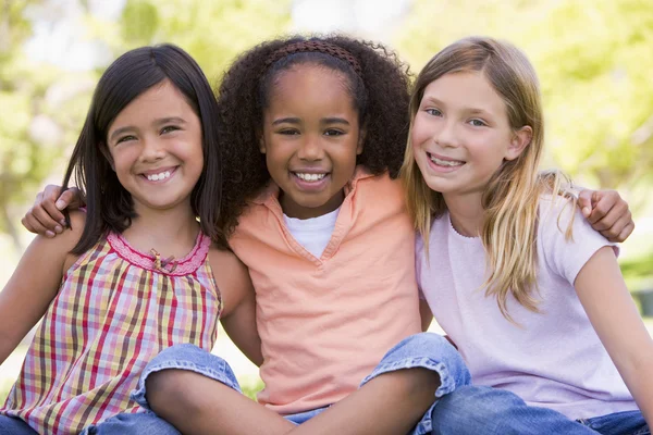 Drie jonge meisje vrienden zitten buiten glimlachen — Stockfoto