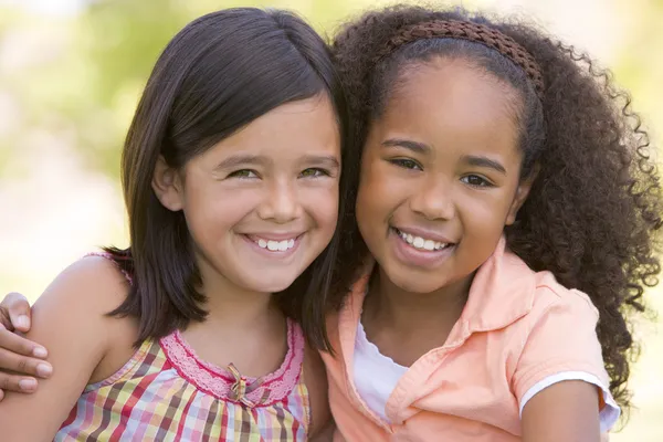 Two young girl friends sitting outdoors smiling — Stock Photo, Image