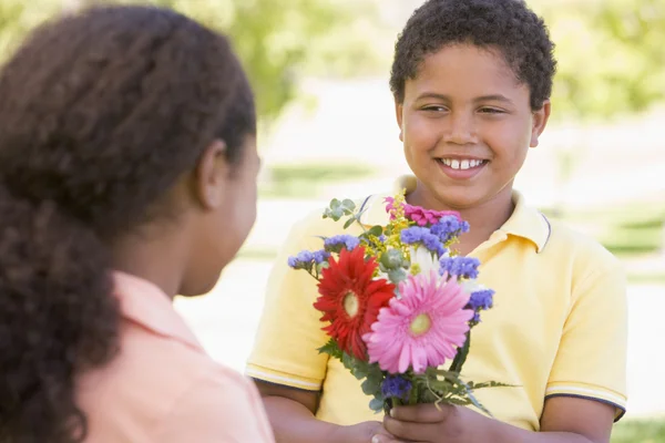 Ung pojke ger ung flicka blommor och ler — Stockfoto