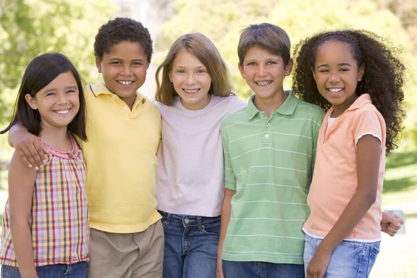 Pięć młodych przyjaciół, stojący na zewnątrz uśmiechający się — Zdjęcie stockowe