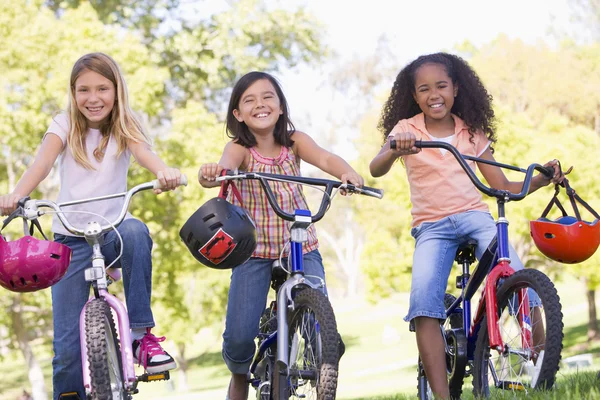 Tre unga flicka vänner utomhus på cyklar leende — Stockfoto