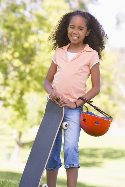 Молодая девушка со скейтбордом на открытом воздухе улыбается — стоковое фото