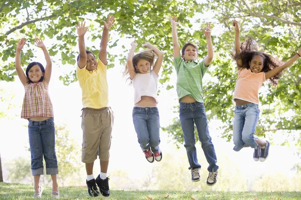 Five young friends jumping outdoors smiling — Stock Photo, Image
