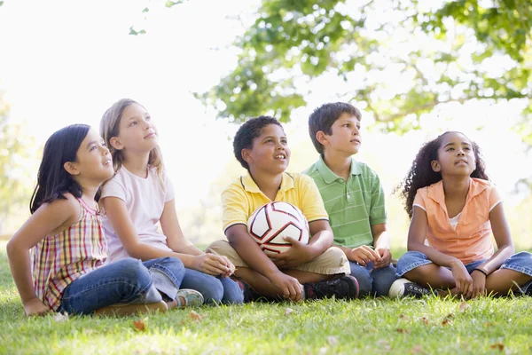 5 个年轻的朋友坐在户外与足球球看 — 图库照片