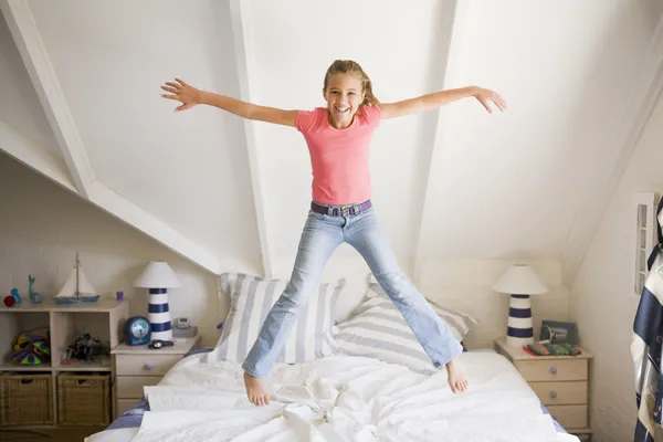 Jong meisje springen op haar bed — Stockfoto