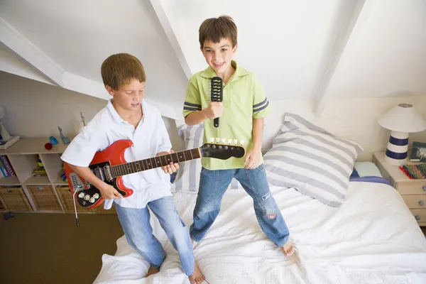 Two Boys Standing On A Bed, Playing Guitar And Singing Into A Ha — Stock Photo, Image