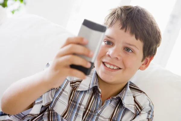 Menino jovem sentado em um sofá mensagens em um telefone móvel — Fotografia de Stock