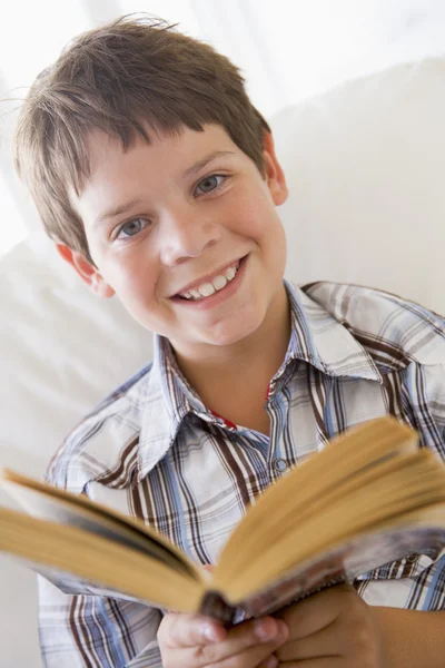 年轻的男孩坐在沙发上读一本书 — 图库照片