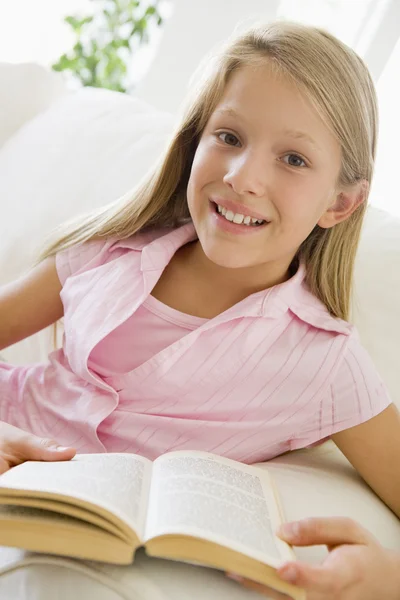 Νεαρό κορίτσι καθμένος σε έναν καναπέ, διαβάζοντας ένα βιβλίο — Φωτογραφία Αρχείου