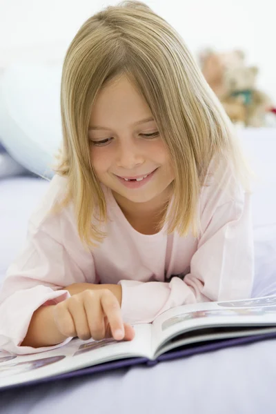 本を読んで彼女のパジャマを着て 彼女のベッドに横になっている若い女の子 — ストック写真