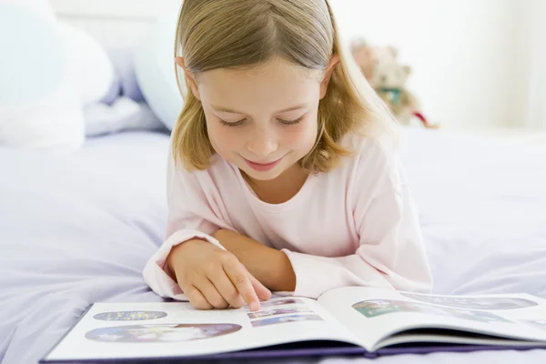 Mladá dívka ležela na posteli v pyžamu, čtení knihy — Stock fotografie