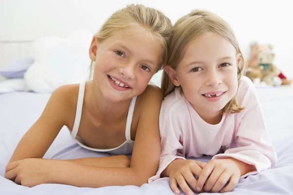 Twee jonge meisjes in hun pyjama's liggend op een bed — Stockfoto