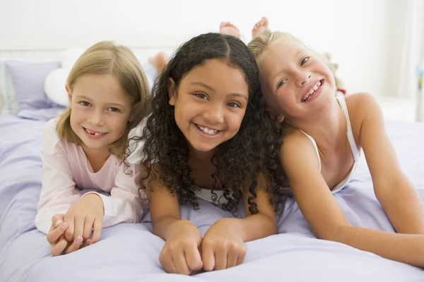 Tre unga flickor liggande på en säng i sin pyjamas — Stockfoto