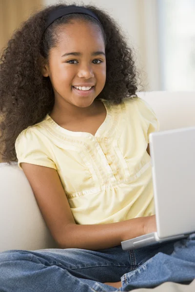 Chica joven sentada en un sofá, usando una computadora portátil — Foto de Stock