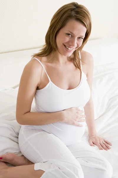 Έγκυος γυναίκα που κάθεται στο κρεβάτι χαμογελώντας — Φωτογραφία Αρχείου