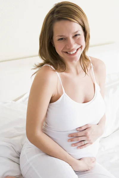 Έγκυος γυναίκα που κάθεται στο κρεβάτι χαμογελώντας — Φωτογραφία Αρχείου