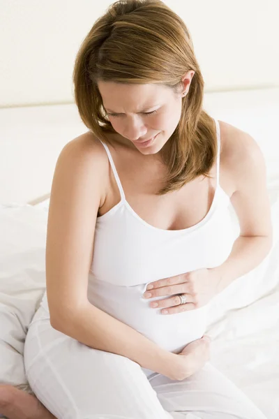 Pregnant woman sitting in bed holding stomach in pain — Stock Photo, Image