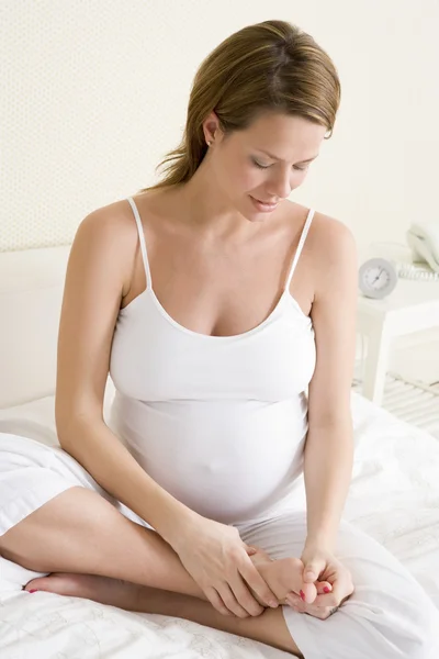ベッドの足をこすりに座って妊娠中の女性 — ストック写真