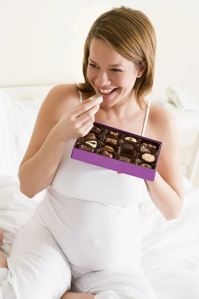 Gravid kvinna i sängen äta choklad leende — Stockfoto