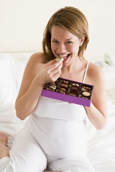 怀孕的女人在床上吃巧克力微笑 — 图库照片