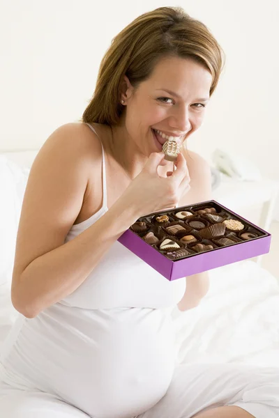 Mujer embarazada en la cama comiendo chocolate sonriente — Foto de Stock