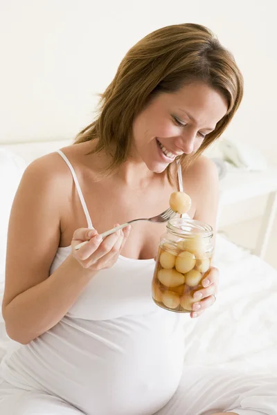 Gravid kvinna i sängen äta inlagda ägg leende — Stockfoto