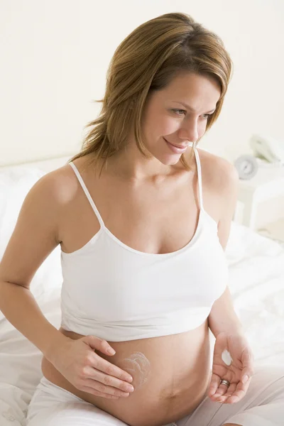 Pregnant woman in bedroom rubbing cream on belly smiling — Stock Photo, Image