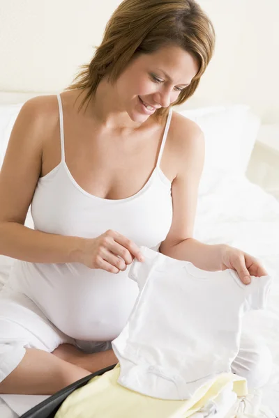 Mulher grávida embalando roupas de bebê na mala sorrindo — Fotografia de Stock